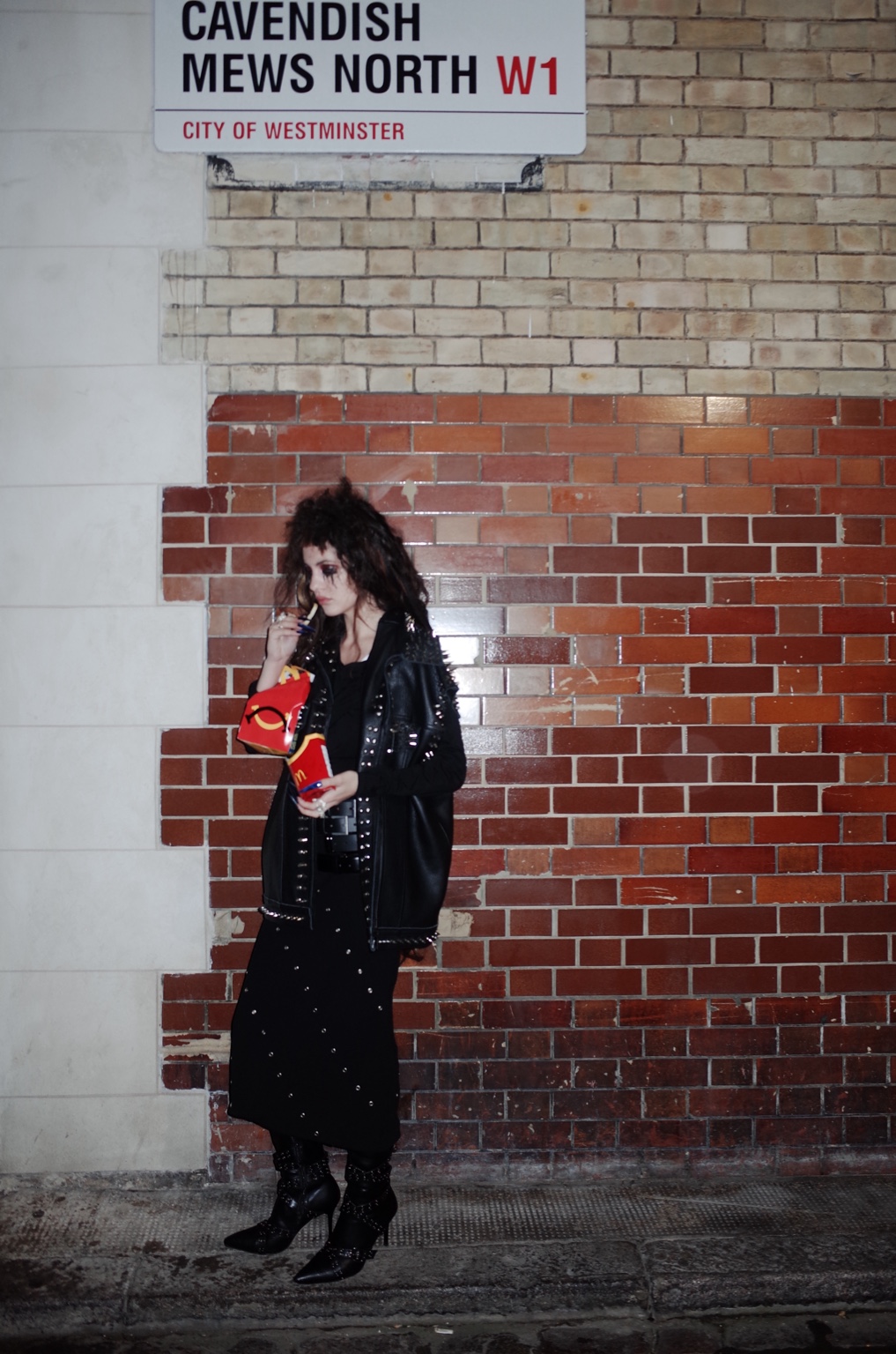 Among Others, figure eating McDonald's beside a brick wall in London