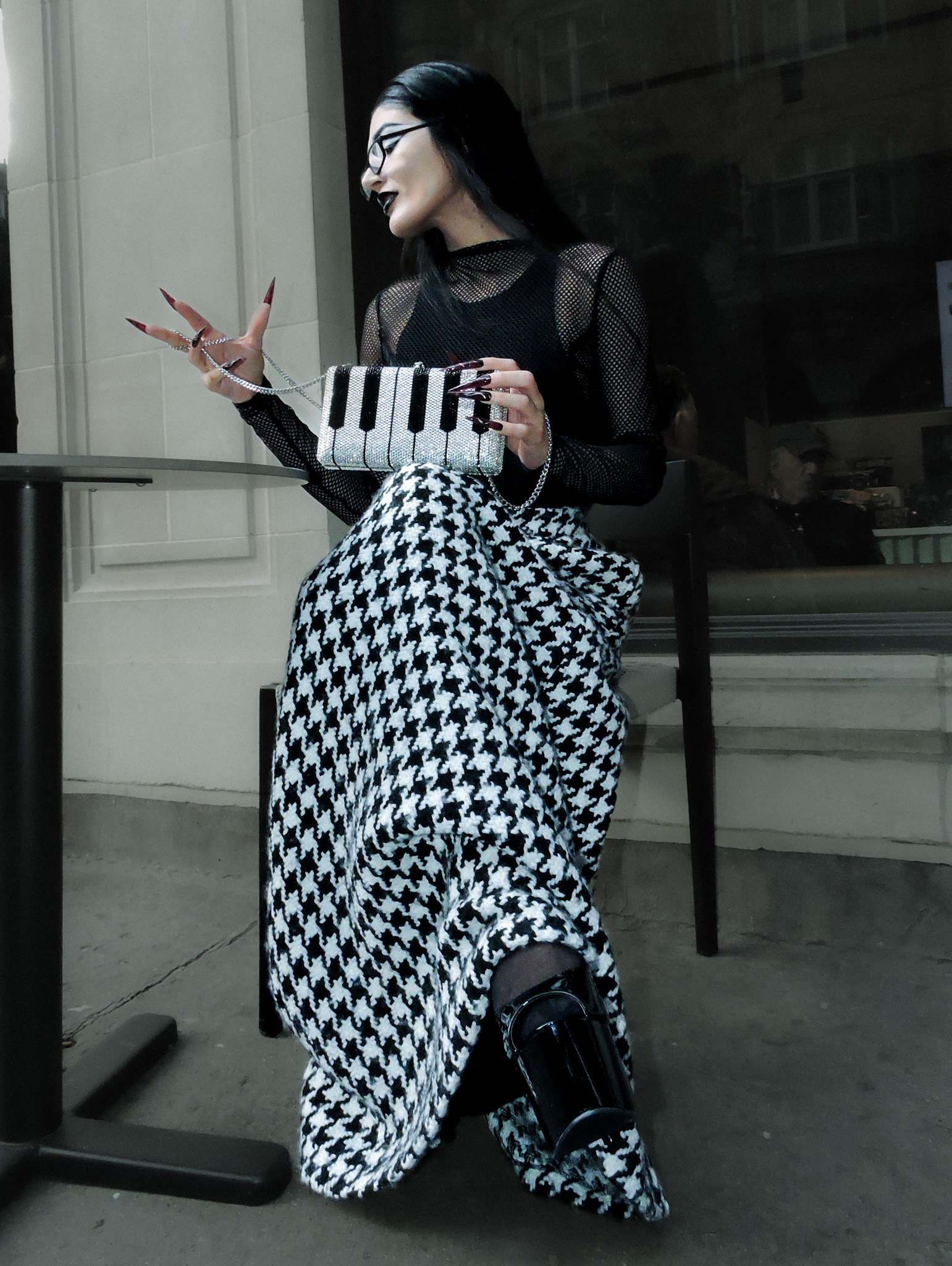 Her Spell, seated figure in black mesh and houndstooth clothing holding a piano-key handbag