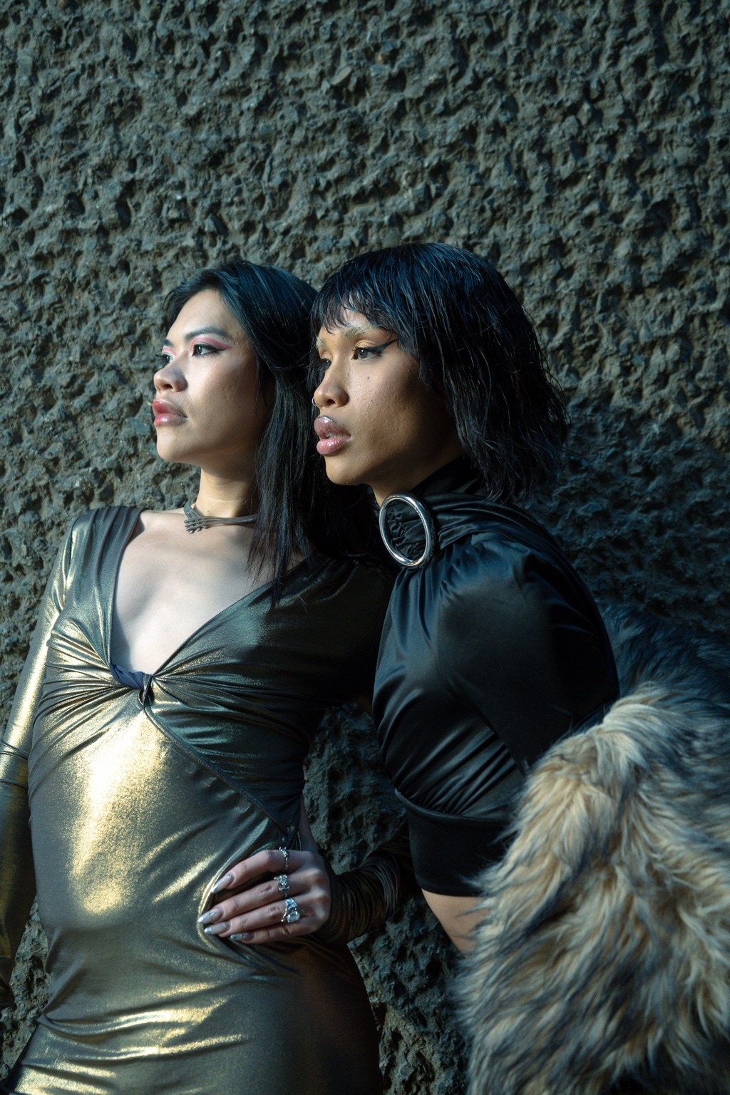 Two dressed figures against a rough concrete wall