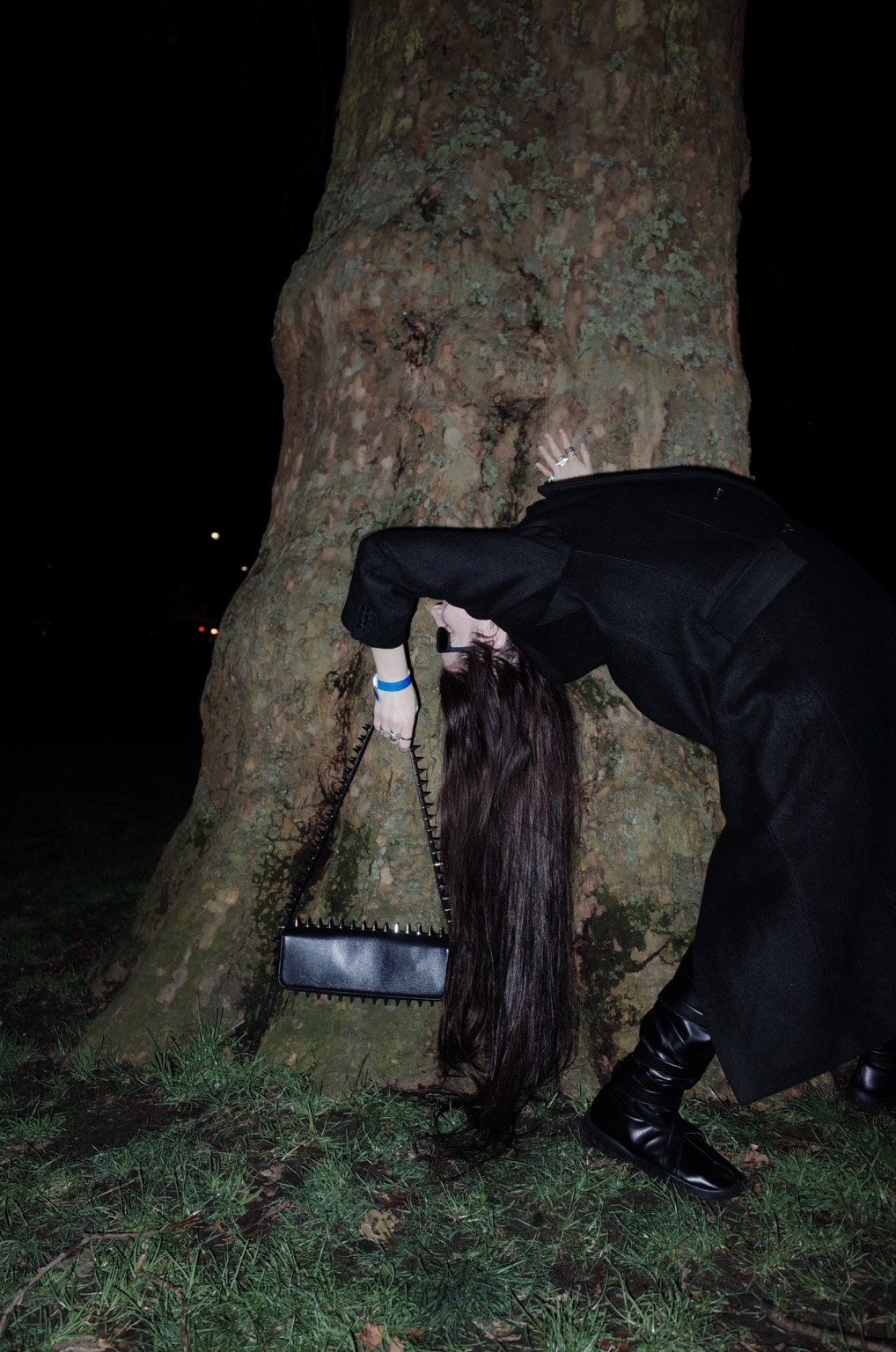 Dressed body bending against a tree at night, London, 16 February 2024