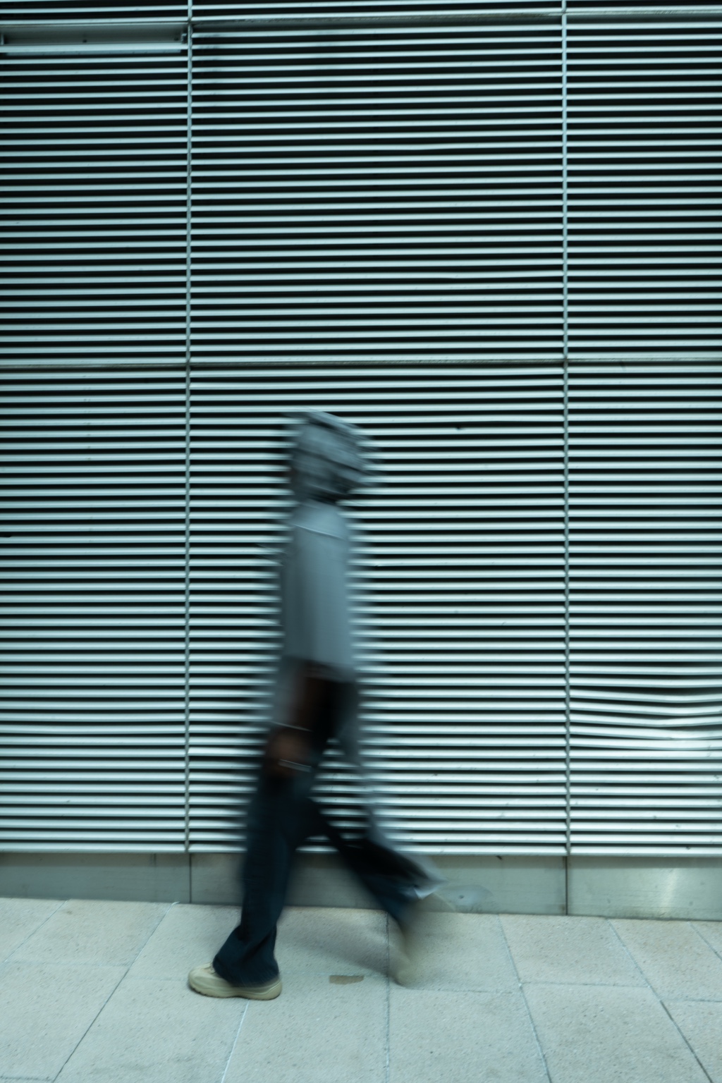 Blurred walking figure against a gridded wall, London, 26 April 2024